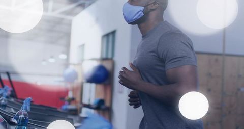 Running on treadmill wearing face mask in modern fitness center with sanitizer
