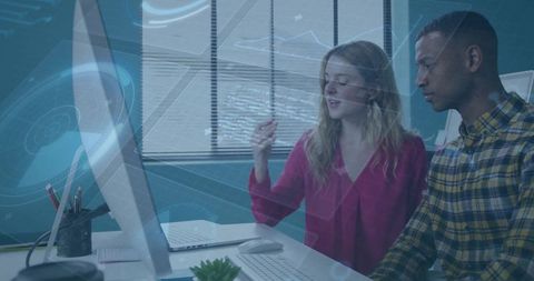 Two colleagues collaborating over holographic data on desktop monitor in modern office