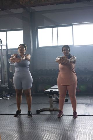 African american women exercising together in gym performing standing arm stretch