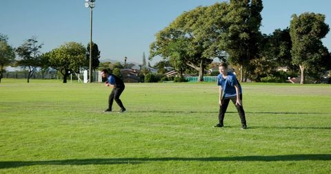 Two young players waiting on sunlit suburban sports field in blue jerseys during practice
