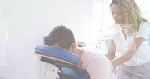 Therapist giving seated massage to male client on blue chair in bright wellness clinic
