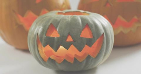Glowing gray-green jack-o-lantern on white tabletop with candlelit grin and textured ridges