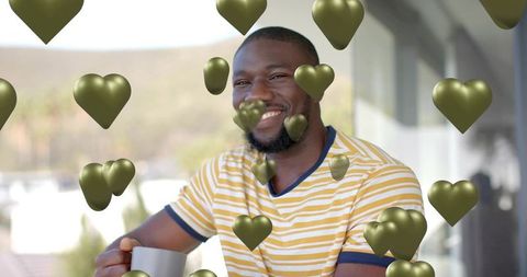 Smiling man holding gray mug on balcony, enjoying coffee with metallic heart overlay