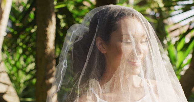 This image features a bride smiling happily, wearing a wedding veil, amidst lush green plants. The outdoor, nature-centric environment can be used for content related to weddings, romance, outdoor ceremonies, and bridal fashion. Suitable for wedding blogs, photography portfolios, online wedding guides, and bridal themed advertisements.