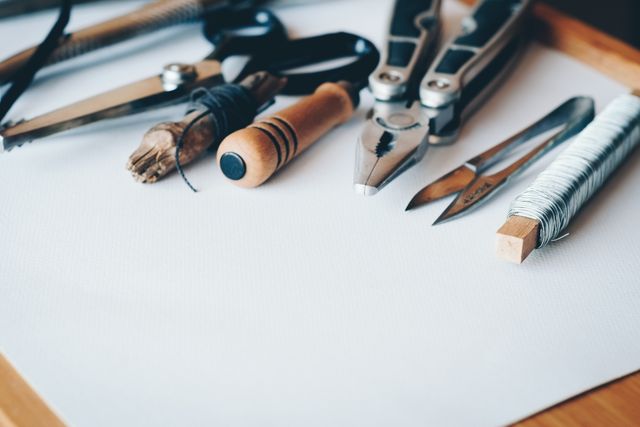 Various crafting and repair tools including scissors, pliers, and cord are neatly arranged on a wooden surface. This image can be used for publications or websites focusing on DIY projects, crafting ideas, home repairs, hobby workshops, and detailed guides on using tools.