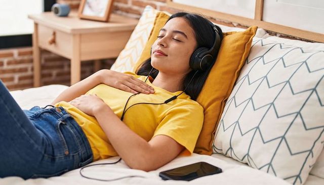 Young woman relaxing on bed listening to music with headphones and smartphone