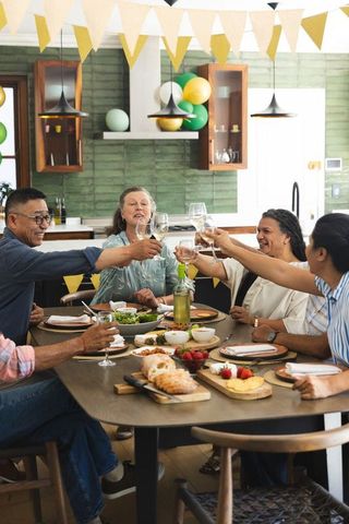 Mature friends and family toasting wine glasses around dining table with festive bunting