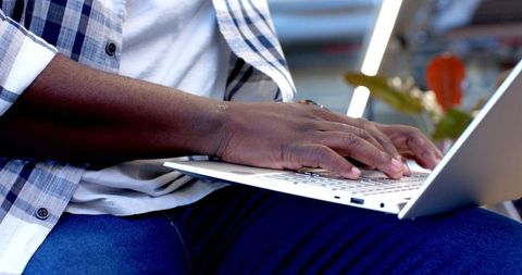 Showcases a young African American male in a plaid shirt working intently on a laptop, ideal for illustrating themes of productivity and technology in modern office settings. Suitable for use in articles or advertisements about workplace efficiency, remote work, or digital projects.