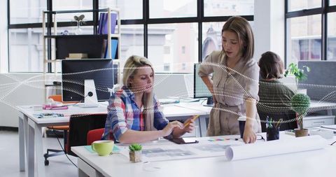 Collaborating on architectural plans in modern open office with tablet and blueprints