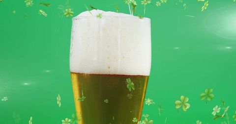 Pilsner glass amber beer with frothy head and floating green shamrocks for st patrick's day