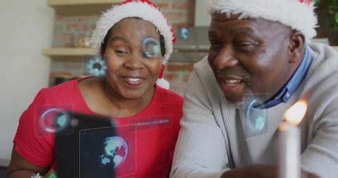 Black senior couple wearing santa hats enjoying tablet with holographic globe overlay
