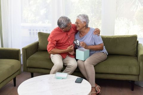 Senior couple sharing joyful ultrasound surprise on sofa while opening keepsake gift