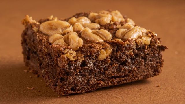 Nut-topped chocolate brownie square with glossy peanut caramel topping close-up