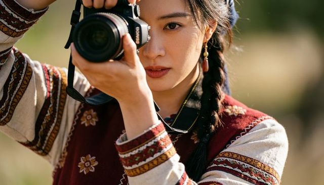 Asian female photographer framing dslr portrait in sunlit meadow with embroidered top
