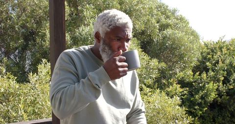 Senior Man Sipping Beverage Outdoors Among Greenery