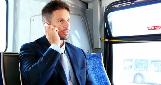 Businessman in formal attire talking on a smartphone while commuting on a bus. This image depicts a professional balancing business communication with travel. Perfect for advertising business services, transportation services, or work-life balance themes.