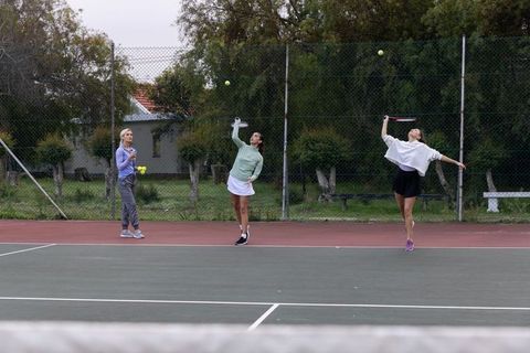 Three women practicing tennis serves on outdoor club court during casual training