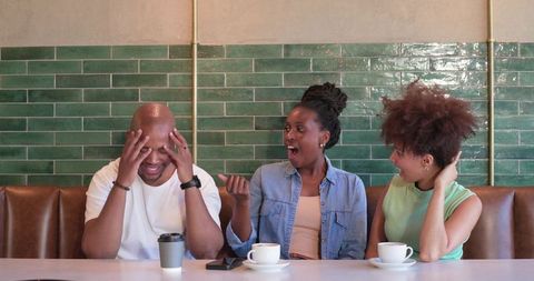 Friends reacting to surprising news over coffee in cafe with green tiles and leather booth