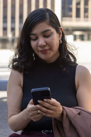 Professional woman checking smartphone in urban plaza during workday commute