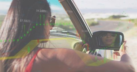 Driver checking side mirror on coastal road with overlaid digital analytics and graphs