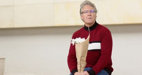 Pensive mature man holding daisies sitting in minimalist lobby wearing red sweater