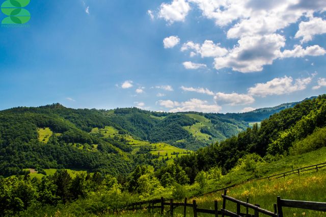 A picturesque summer scene featuring rolling hills covered in green flora under a clear blue sky with white clouds. Ideal for use in travel brochures, nature calendars, and scenic backgrounds to promote outdoor activities, tourism, and relaxation in natural settings.