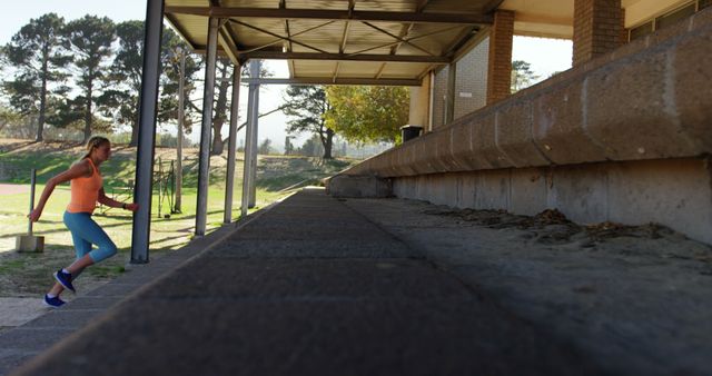 A young woman is seen running up a set of outdoor stairs on a college campus, emphasizing an active lifestyle and fitness. The background consists of greenery and trees. This image is ideal for promoting health and fitness, college lifestyle, outdoor activities, sports motivations, or physical education. It can be used for advertisements, blogs, and websites focusing on wellness, student life, or outdoor exercises.