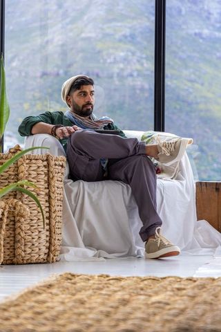 Indian man relaxing on slipcovered armchair by large window with mountain view
