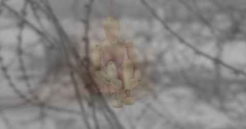 Wooden puppet sitting behind barbed wire amid fog