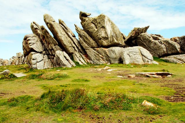 Eroded granite rock formation standing amid a vibrant grassy field under a blue sky. Ideal for use in content related to geology, nature exploration, outdoor adventures, environmental science, and travel destinations. The unique rock structures provide visual interest and convey a sense of natural beauty and timelessness.