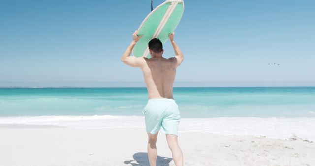 Young Male Surfer Carrying Surfboard Towards Ocean on Bright Sunny Beach - Download Free Stock Images Pikwizard.com