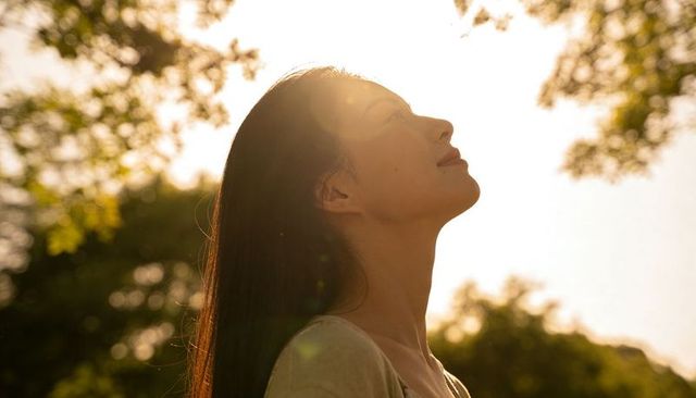 Woman soaking in golden hour sunlight in park backlit profile with lens flare