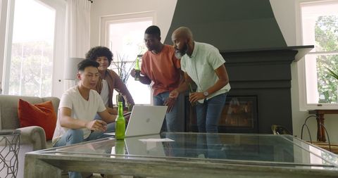 Diverse Friends Socializing in Living Room with Laptop and Drinks