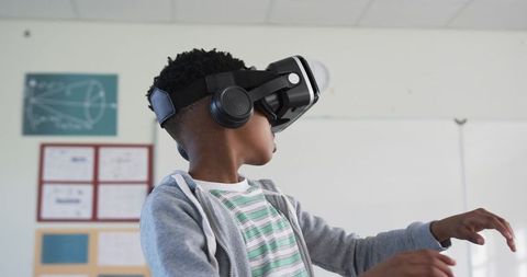 Student wearing VR headset and headphones reaching forward in classroom exploring virtual reality