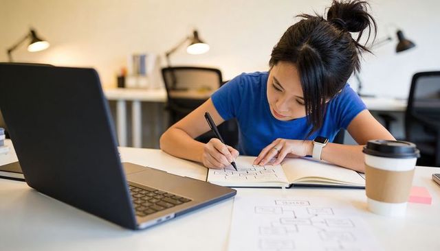 Young professional sketching wireframes and diagrams at laptop in modern coworking desk