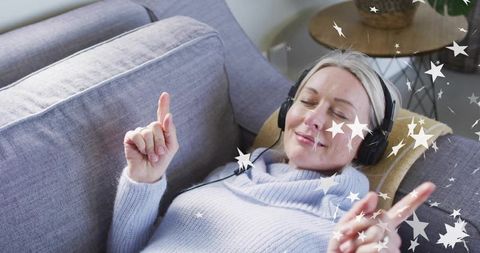 Mature Woman Relaxing with Headphones on Cozy Sofa Amid Starry Overlay