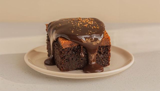 Decadent chocolate brownie dripping ganache with golden crumbs on beige plate
