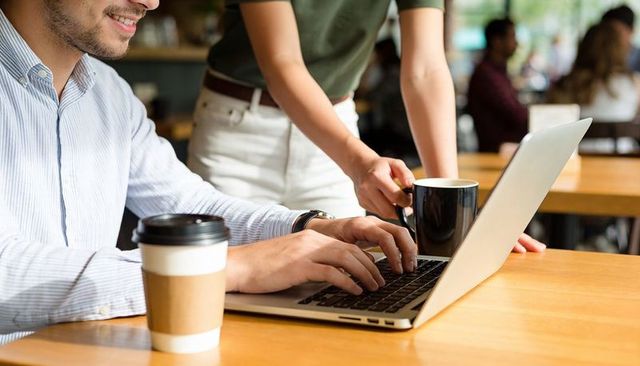 Young professionals collaborating over laptop and coffee in sunlit cafe workspace