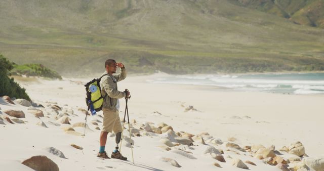Fit biracial man with prosthetic leg, enjoying his time on a trip to the mountains, hiking, walking on the beach, using Nordic walking sticks, protecting his eyes from the sun, looking away