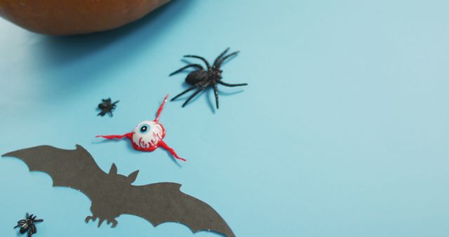 Secrets and creepy Halloween decor including a bat, spider, and fake eyeball on a blue surface. Perfect for Halloween party invitations, spooky holiday greeting cards, festive decorations, or themed social media posts celebrating the holiday.