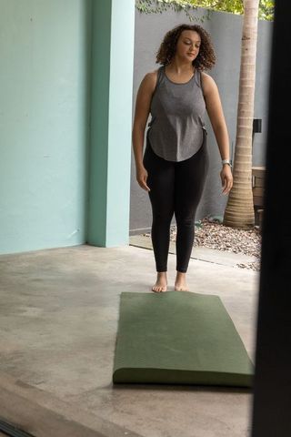 African american woman standing barefoot on green mat preparing for yoga and home workout