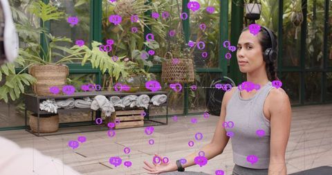 Meditating woman practicing mindfulness in greenhouse wearing wireless headset and smartwatch