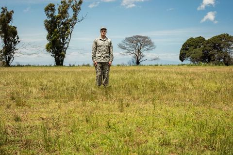 Soldier standing centered in wide open grassland wearing camouflage uniform and cap