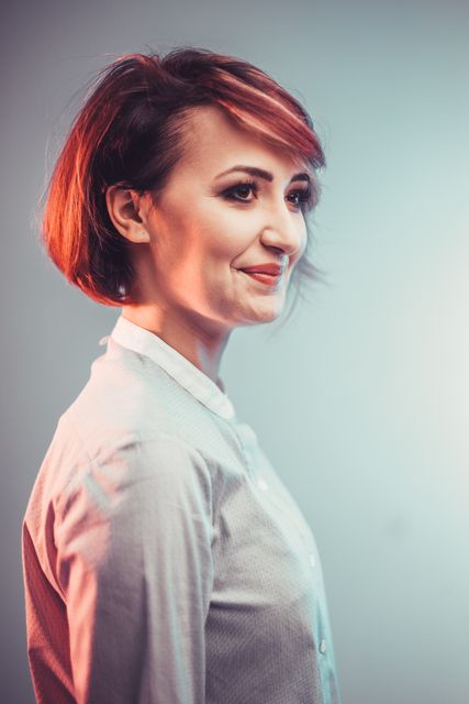 This stock photo shows a confident young woman with a short modern hairstyle, dressed in professional attire. Standing against an isolated background, she is smiling with a side profile view. Ideal for use in professional business contexts, career exemplifications, or fashion portfolio presentations.
