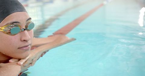 Young female swimmer resting at edge of indoor pool