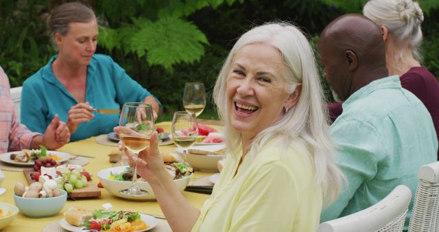 Image of happy caucasian senior woman eating lunch in garden with diverse friends. retirement lifestyle, spending quality time with friends.