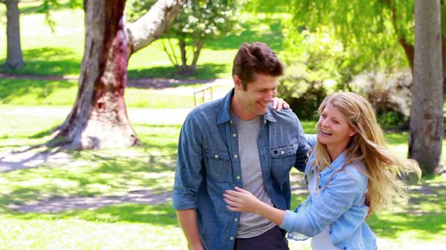 Young couple enjoying each other's company in a green park. Great for advertisements promoting romance or lifestyle blogs focused on relationship advice. Scene captures fun, love, and carefree spirit, ideal for social media campaigns or articles about spending quality time outdoors.