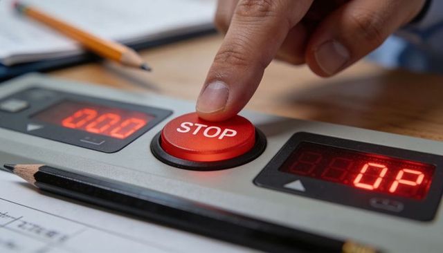 Finger pressing red stop button on control panel with digital timers and office supplies