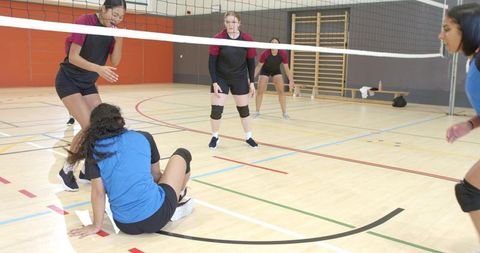 Diverse female volleyball team competing in indoor gym with indian player sitting by net