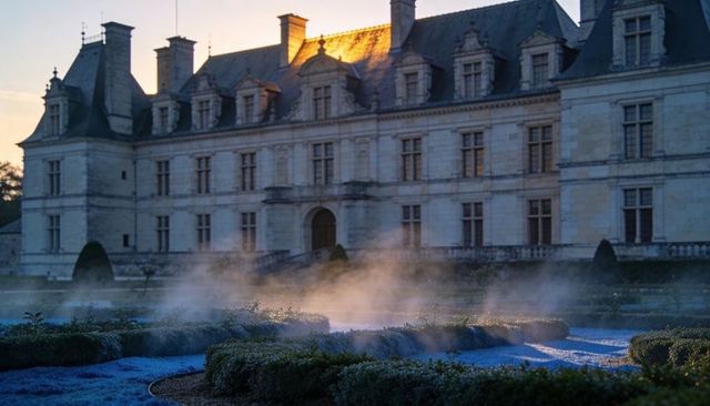 Sunrise light bathing limestone chateau with formal parterre and ethereal garden mist
